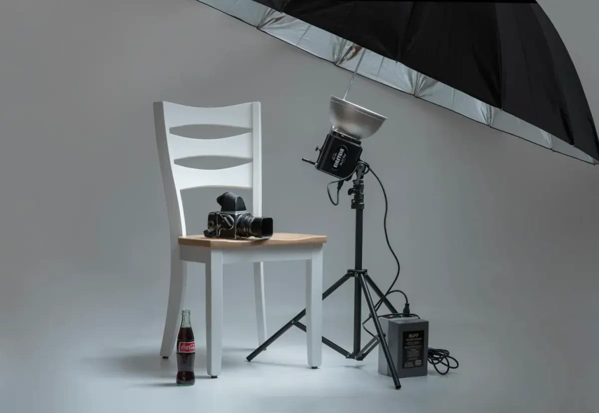 Black video camera on white wooden chairs beside photo shooting umbrella